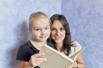 Cute smiling daughter are reading a book with her mother