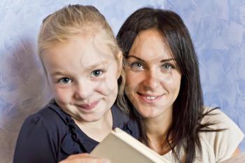 Cute smiling daughter are reading a book with her mother