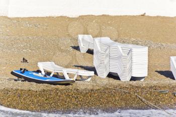 Empty beach with sun loungers and surfboard in summer day