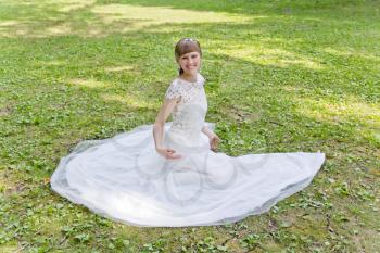 Beautiful bride in white lace dress sitting on green grass