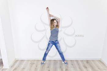 Girl eleven years old with blond hair standing near white wall and upwards hands