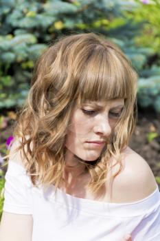 Vertical portrait of sad woman with blond hair on summer background