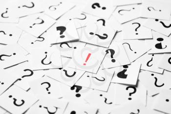 Pile of question mark signs scattered around with one red exclamation symbol in the center. Decision, enquiry or faq concept.