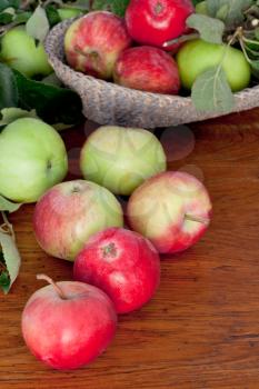 many red and green apples with leaves on wooden table close up