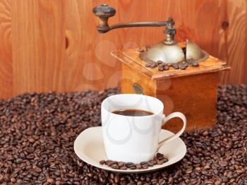 cup of coffee and roasted coffee beans with retro manual mill near wooden wall