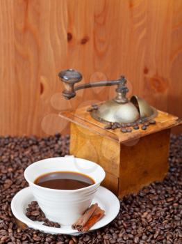 cup of coffee and roasted coffee beans with retro wooden manual mill, cinnamon