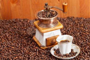 small cup of coffee and roasted coffee beans with retro copper manual mill and wooden wall