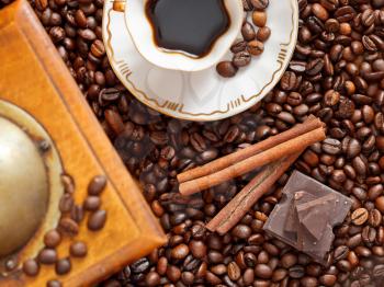 top view small cup of coffee and roasted coffee beans with retro wooden manual mill, cinnamon, chocolate bars close up