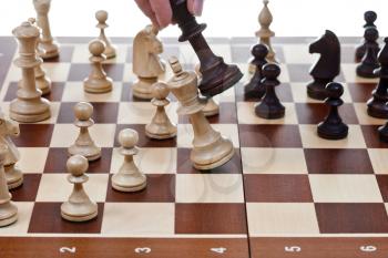 hand with black king hits white king on chessboard in chess game