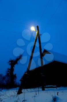 outdoor electric lantern under rural house in dark blue winter evening