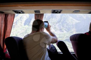 Tourist takes on smartphone mountain scenery outside bus