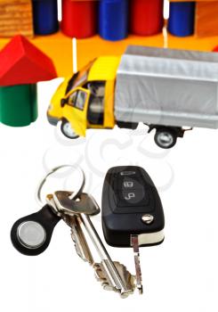 above view of door keys, vehicle key, new truck model and wooden block toy house isolated on white background