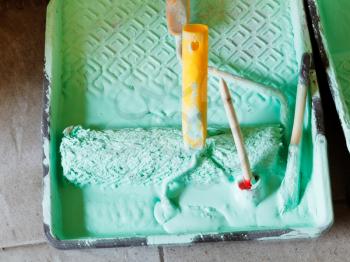 plastic paint tray with green emulsion paint and paintbrushes