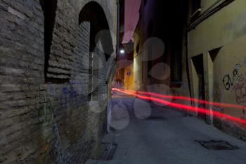 narrow medieval street in Bologna and car red headlights at night, Italy