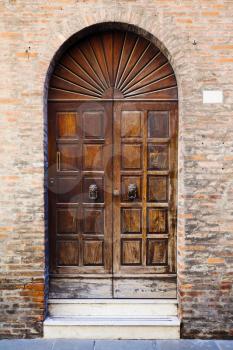 wooden door in brick wall of medieval house in Ferrara, Italy