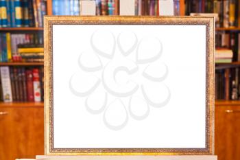 white canvas of picture frame on easel with clipping path and home library on background