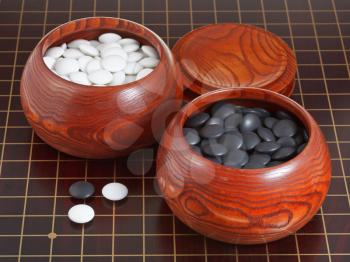 black and white go game stones and wooden bowls on wooden goban