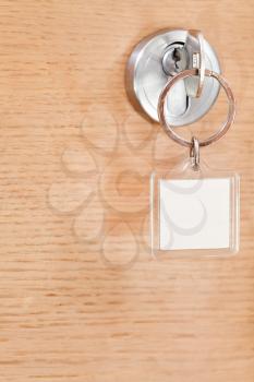 steel key with blank square keychain in lock of wooden door