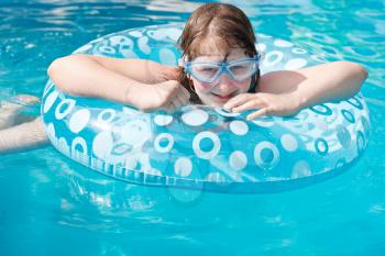 girl in swim goggle on inflatable circle in blue open-air pool