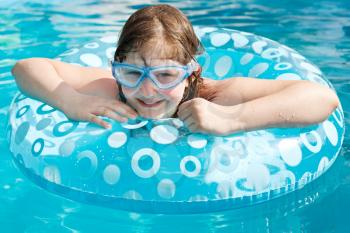 girl in swim goggle on swimming circle in blue open-air pool