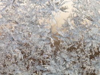 snowflakes and frost on glass close up - frosty brown blue pattern on window in cold winter day