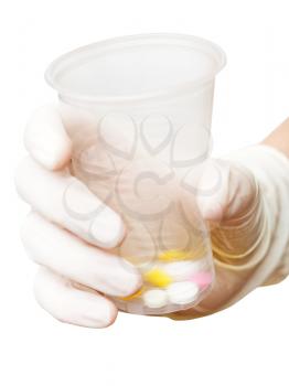 gloved hand holding plastic cup with pills isolated on white background