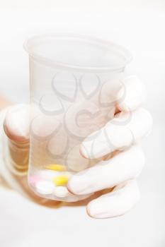 gloved hand holding plastic cup with pills on white background