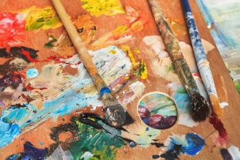 paintbrushes on wooden artistic palette on picture canvas