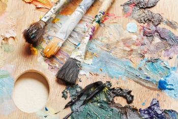 three used paint brushes on wooden artistic pallette