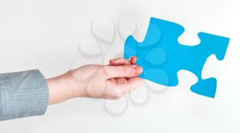 blue puzzle piece in female hand on grey background