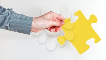 female hand holding yellow puzzle piece on grey background