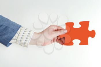 male hand holding red puzzle piece on grey background