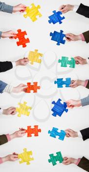 set painted puzzle pieces in people hands on grey background