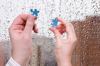 male and female hands with little puzzle pieces with home window and rain drops background
