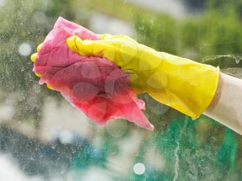 hand in yellow rubber glove cleaning window glass by wet rag