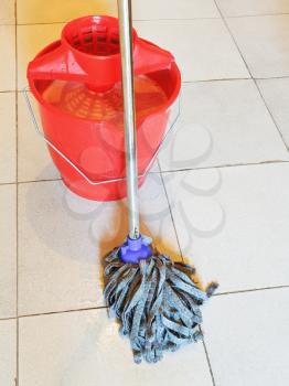red bucket with foamy water and mopping the tile floors