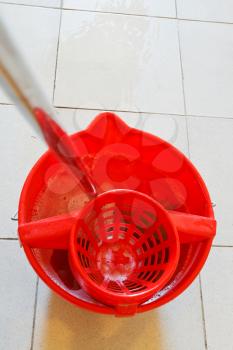 mop in red bucket with foamy water on tile floor