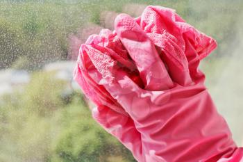 hand in pink rubber glove washing window glass by wet cloth