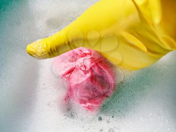 hand in yellow rubber glove wrings out wet cloth from foamy water