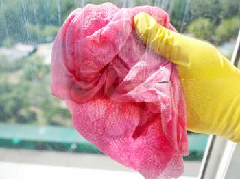 hand in yellow rubber glove cleaning window glass by wet cloth