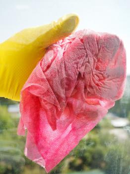 hand in yellow rubber glove washing window glass by wet duster