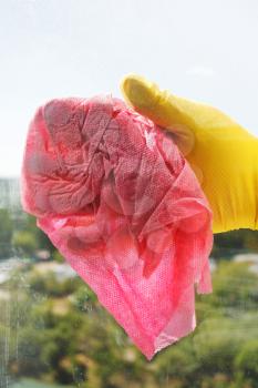 hand in yellow rubber glove washing window glass by wet rag