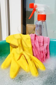 home window washer set - rubber glove, wet cloth, spray cleaner bottle, soapy water in green basin on sill