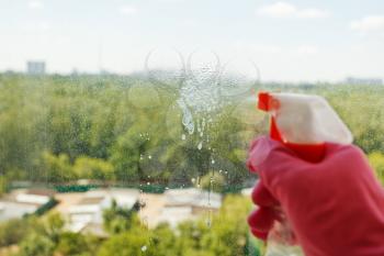 washing home window - liquid jet from spray bottle on glass with green park outside