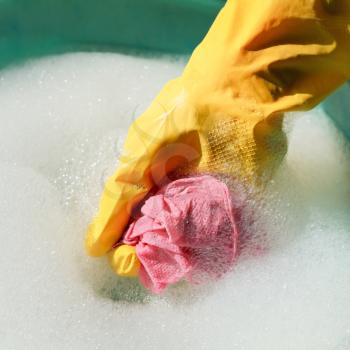 hand in yellow rubber glove rinsing wet duster in soapy water