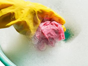 hand in yellow rubber glove rinsing rag in soap suds water