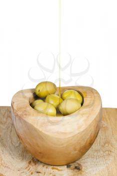 olive oil in thin trickle flows on olives in wooden bowl close up isolated on white background