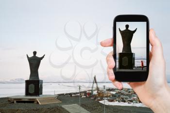 travel concept - tourist taking photo of Monument Saint Nicholas on Andyrsky liman in Chukotka on mobile gadget, Anadyr, Russia
