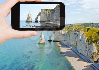 travel concept - tourist taking photo of english channel coast with cliffs on Etretat cote d'albatre, France on mobile gadget