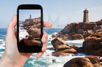 travel concept - tourist taking photo of Lighthouse on Cote de Granite Rose in Brittany on mobile gadget, France